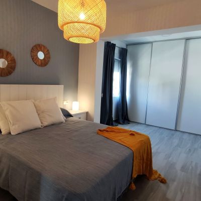 Dormitorio moderno con cama de matrimonio, cabecero blanco, manta mostaza, armario empotrado y luz cálida.