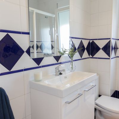 Baño con azulejos blancos y azules, lavabo moderno con mueble de almacenaje, espejo y decoración minimalista.