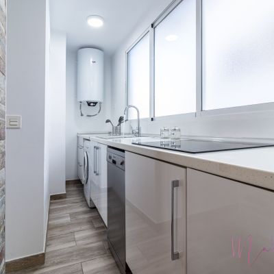 Cocina moderna y luminosa con muebles blancos, encimera de cuarzo, electrodomésticos de acero inoxidable y paredes con acabado en piedra.