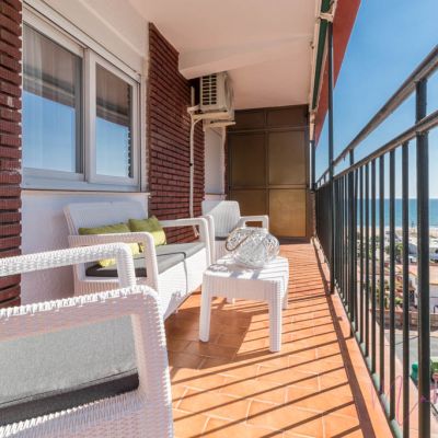 Terraza con muebles de exterior blancos, cojines verdes, suelo de terracota y vistas panorámicas al mar.