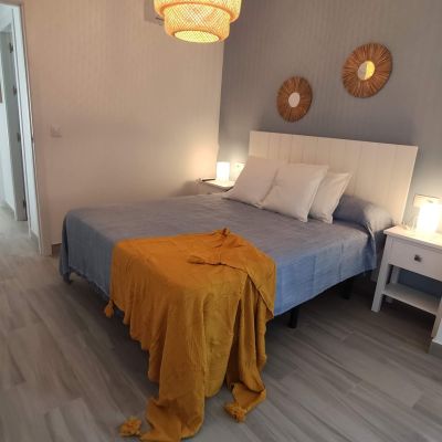Dormitorio moderno con cama de matrimonio, decoración en tonos azules y neutros, manta mostaza y luz cálida.